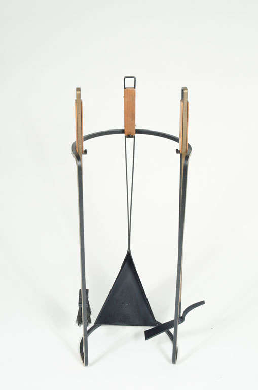 A wonderful Mid-Century Modern set of fire tools comprised of a wrought iron satand in a demi-lune form holding three tools each in wrought iron with triangular wood handles from the 